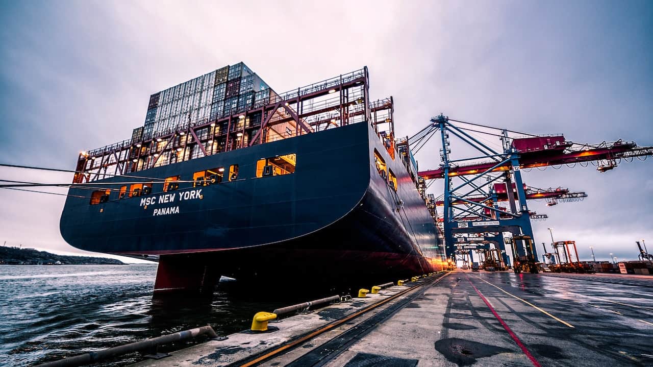 Large cargo ship docked at a bustling industrial port with cranes.