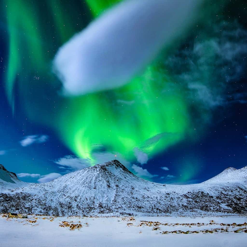 Northern Lights over a snowy mountain landscape with a clear night sky.